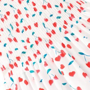 Gros plan sur le motif cerises et cœurs imprimé sur la robe fille blanche.